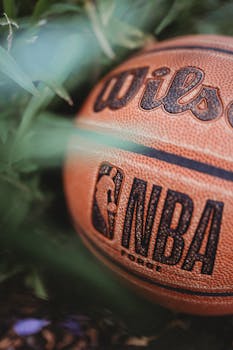 Detailed close-up of a Wilson basketball with NBA logo, surrounded by greenery.