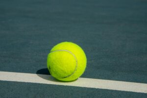 Vibrant yellow tennis ball on a court line, showcasing sports and recreation.