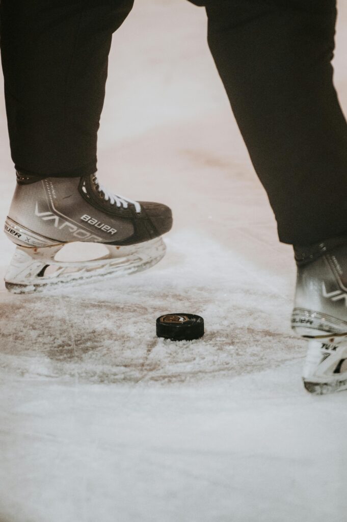 Close-up of ice hockey skates poised above a puck on the rink. Perfect for sports enthusiasts.