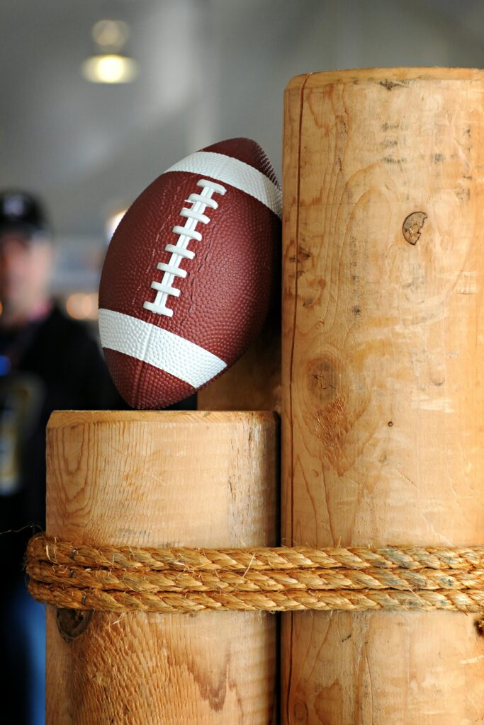 Close-up of a football resting on stacked wooden logs with a rustic rope indoors.