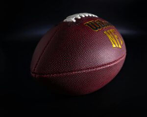 Detailed view of a traditional brown and white American football against a dark backdrop, highlighting texture.